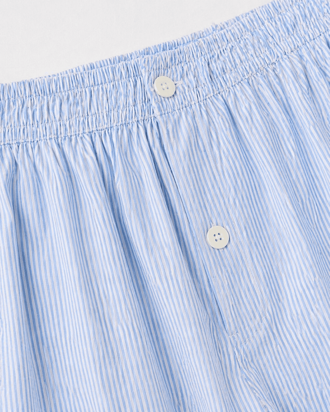 Close-up of light blue striped boxer shorts with button details on a white background