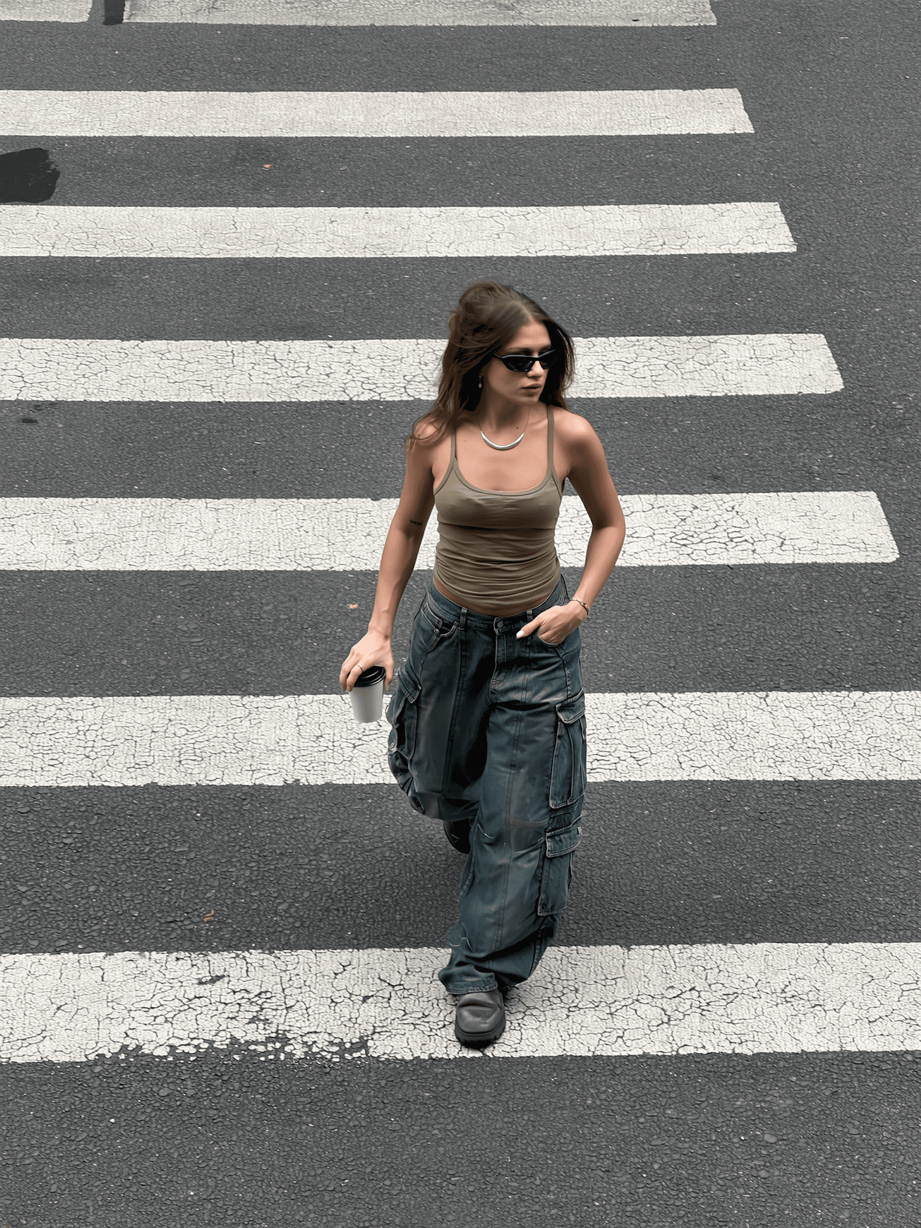 Woman walking on a zebra crossing wearing sunglasses and casual clothing.